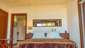 A bedroom with a large bed, a wooden headboard, a bedside table, and a window with a view of greenery.