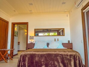 Ein Schlafzimmer mit einem großen Bett, einem Holzkopfende, einem Nachttisch und einem Fenster mit Blick auf Grünflächen.