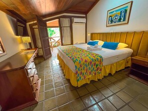 A bedroom with a bed, a bedside table, a lamp, a window, and a door leading to an outdoor area.