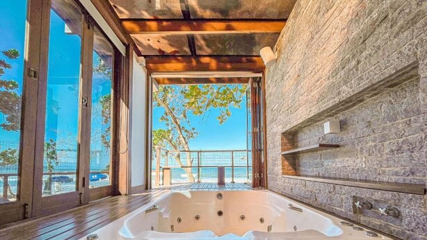 A hot tub in a wooden deck with a stone wall and large windows overlooking a balcony.