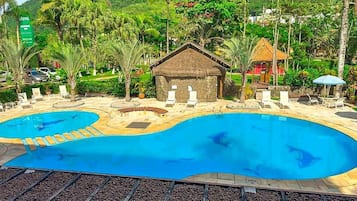A hotel with two swimming pools, a thatched-roof hut, and a tropical garden.