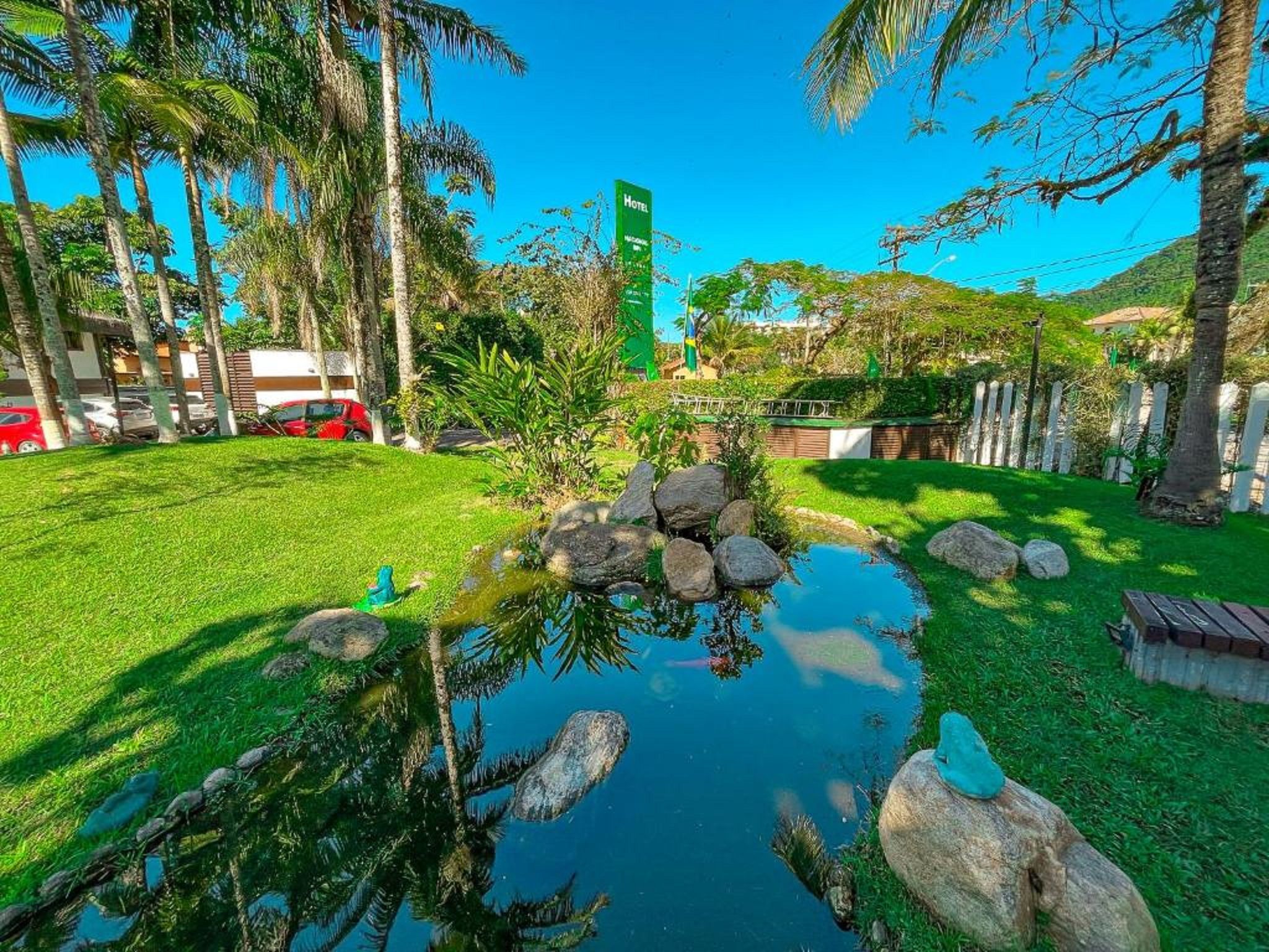 Un exuberante jardín con un estanque, palmeras y un letrero de hotel al fondo.