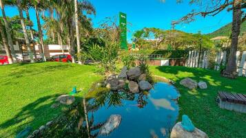 Un exuberante jardín con un estanque, palmeras y un letrero de hotel al fondo.