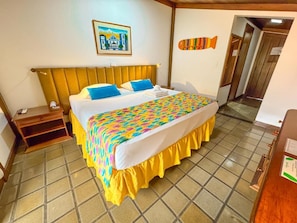 Habitación de hotel con cama, mesita de noche, una decoración de pez montada en la pared, un cuadro enmarcado y una puerta de madera.
