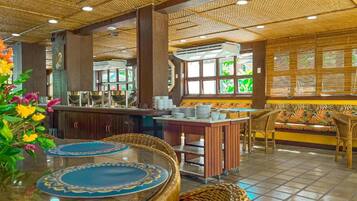 Een restaurant met een tropisch thema, met een bar, zitplaatsen met geweven stoelen en een decoratief plafond.