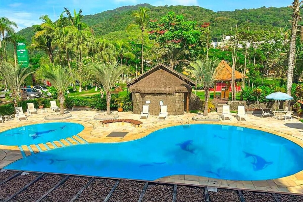 Un hotel con dos piscinas, una cabaña de techo de paja y un jardín tropical.