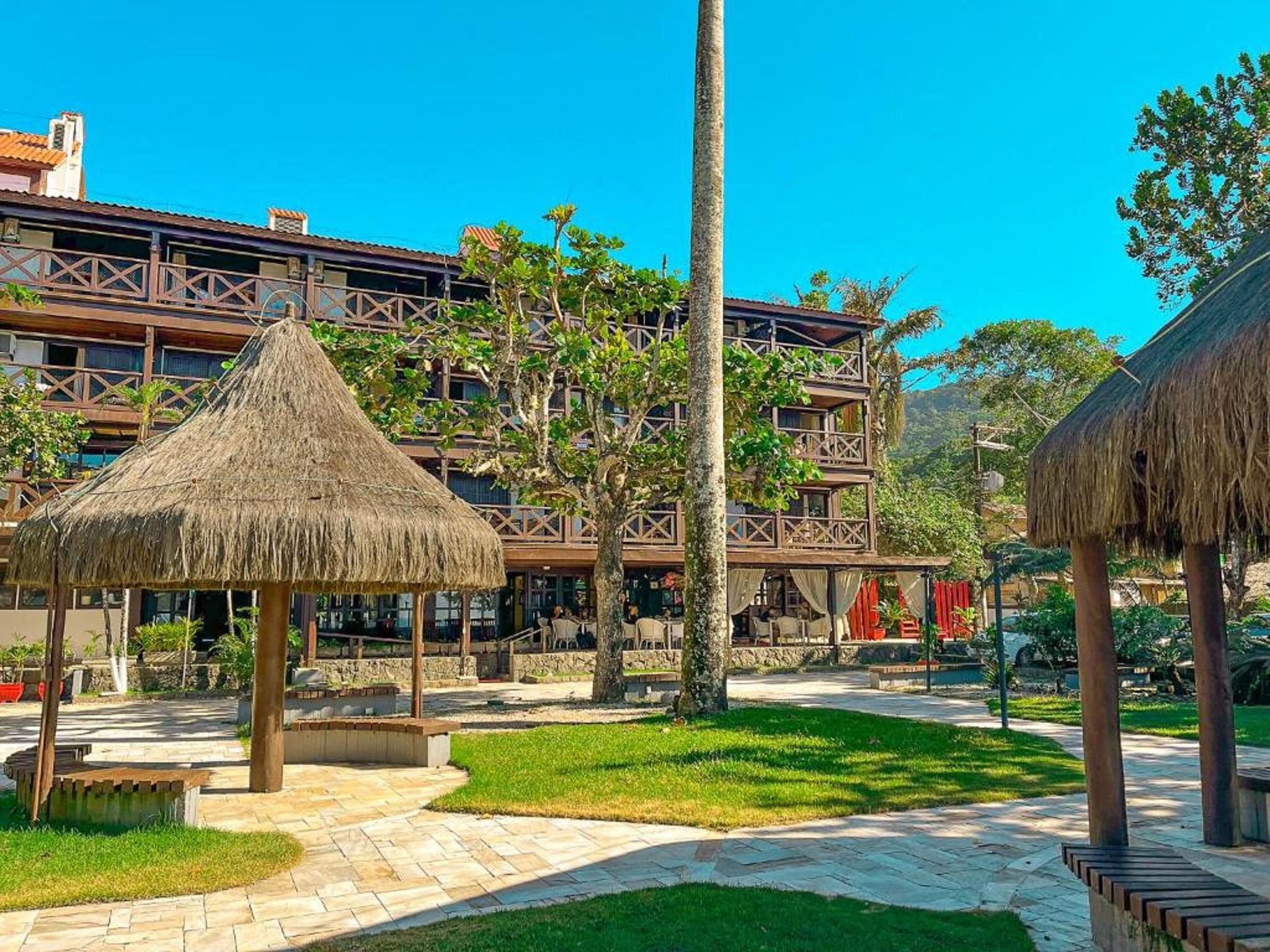 Un resort con un pabellón de techo de paja, un área de piscina y un edificio de varios pisos con balcones.