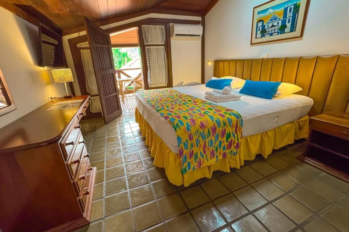 Un dormitorio con cama, mesita de noche, lámpara, ventana y puerta que da a un espacio exterior.
