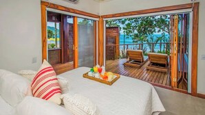 A bedroom with a bed, a tray of fruit, and a view of the ocean through a sliding door.