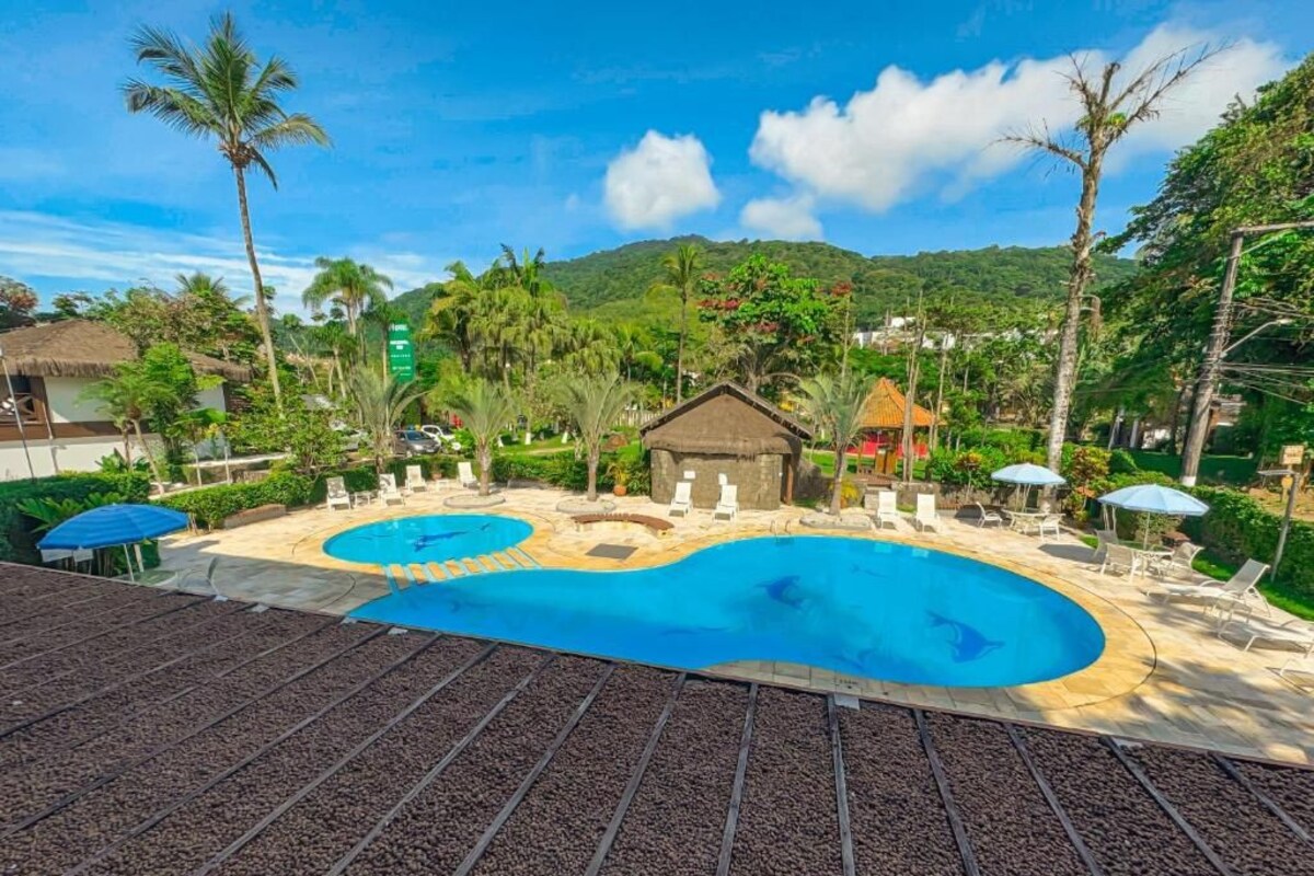 Un resort con una amplia piscina, sillas de descanso y una cabaña con techo de paja.