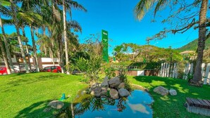 A lush garden with a pond, palm trees, and a hotel sign in the background.