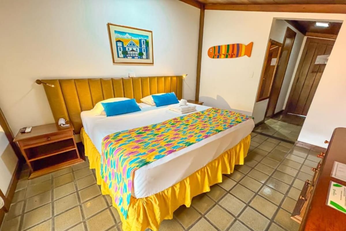 Habitación de hotel con cama, mesita de noche, una decoración de pez montada en la pared, un cuadro enmarcado y una puerta de madera.