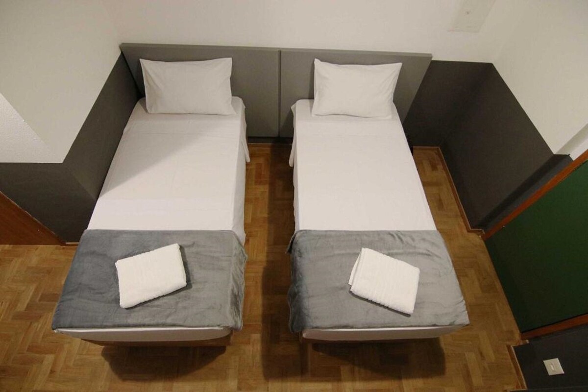 A room with two single beds, each with a grey bedspread and white pillows.