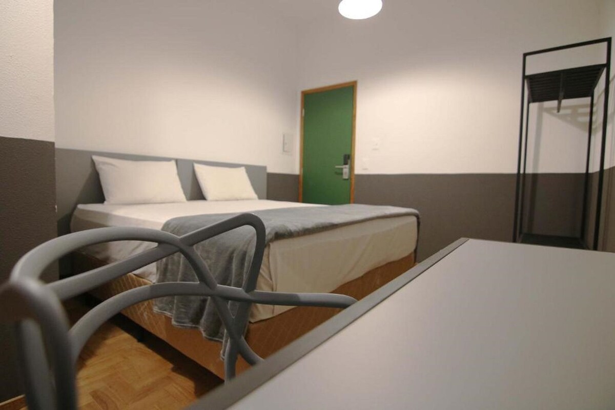 A single bed with a grey headboard, a green door, and a glass partition to the right.