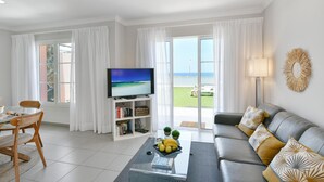 Ein Wohnzimmer mit Fernseher, Sofa, Couchtisch und Meerblick durch große Fenster.