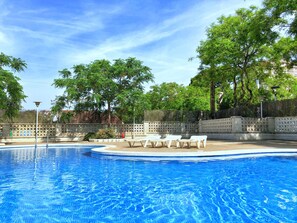 A swimming pool with clear blue water, surrounded by a fence and trees. - Rentalmar Arquus (Salou)