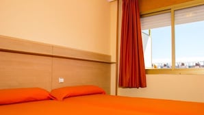 A hotel room with a bed, wooden headboard, and a window with a curtain. - Rentalmar Arquus (Salou)