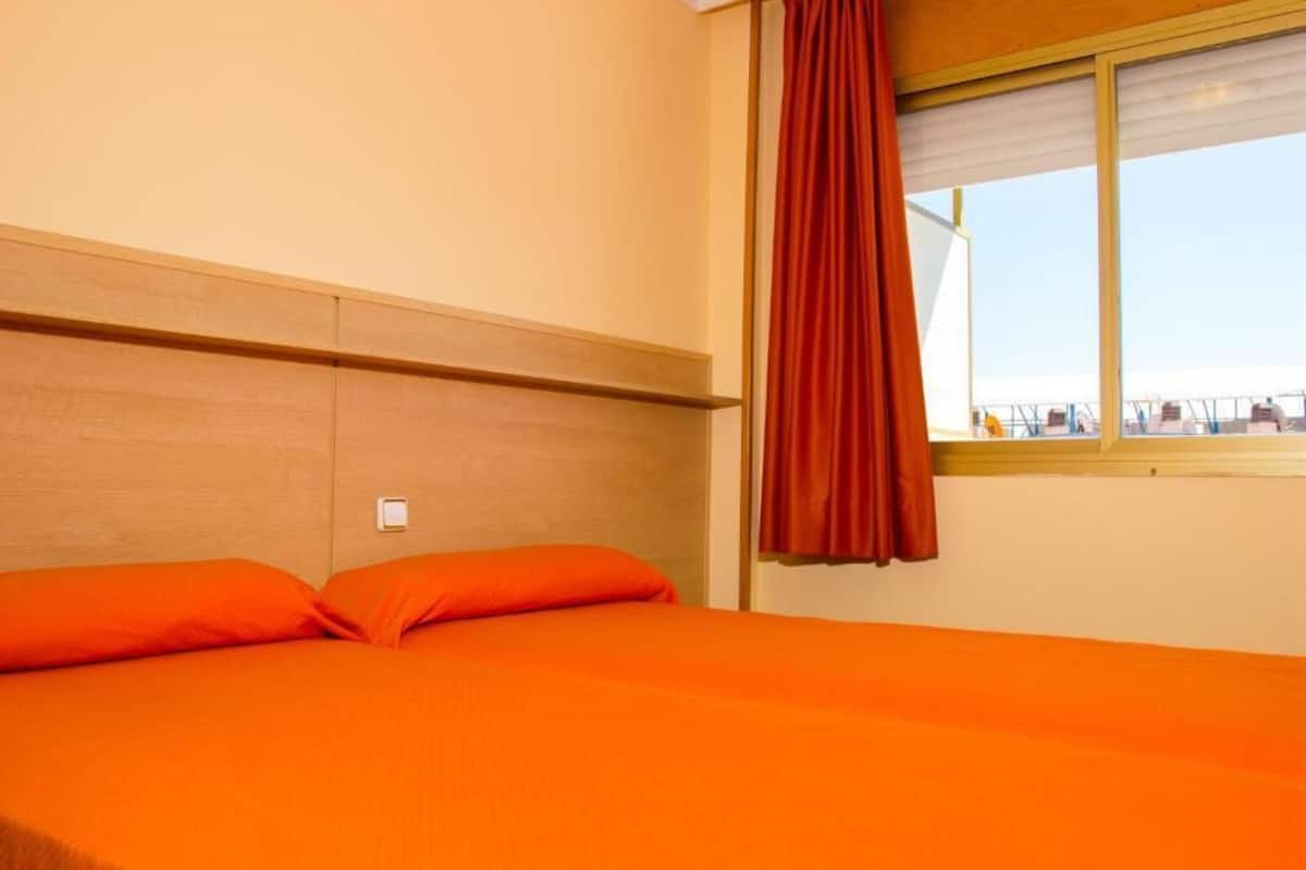 A hotel room with a bed, wooden headboard, and a window with a curtain.