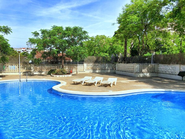 A swimming pool with clear blue water, surrounded by a sandy area with white lounge chairs. - Rentalmar Arquus (Salou)