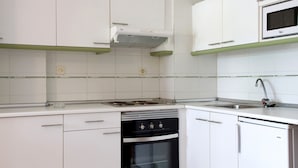 A kitchen with white cabinets, a built-in stove, a microwave, and a sink. - Rentalmar Arquus (Salou)