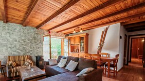 A cozy living room with a stone wall, wooden ceiling beams, a leather sofa, a dining table, and a fireplace. - Apartaments Pleta Bona (La Vall de Boi)