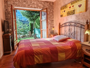 A bedroom with a bed, a TV, a lamp, and a view of greenery outside. - Apartaments Pleta Bona (La Vall de Boi)