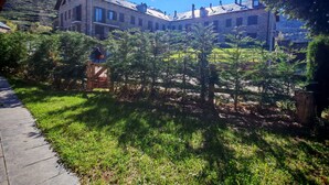 A stone building with multiple windows and a sloped roof, surrounded by greenery and a clear sky. - Apartaments Pleta Bona (La Vall de Boi)