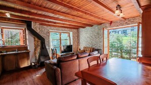 A rustic interior with a wooden ceiling, stone walls, a fireplace, a sofa, a TV, and a dining table. - Apartaments Pleta Bona (La Vall de Boi)