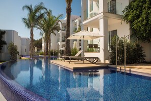 A swimming pool with lounge chairs and umbrellas, surrounded by palm trees and modern buildings. - Insotel Tarida Beach Resort & SPA (Sant Josep de sa Talaia)
