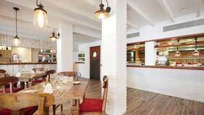 A restaurant with wooden tables and chairs, a bar area, and a kitchen visible through a glass partition. - Insotel Tarida Beach Resort & SPA (Sant Josep de sa Talaia)