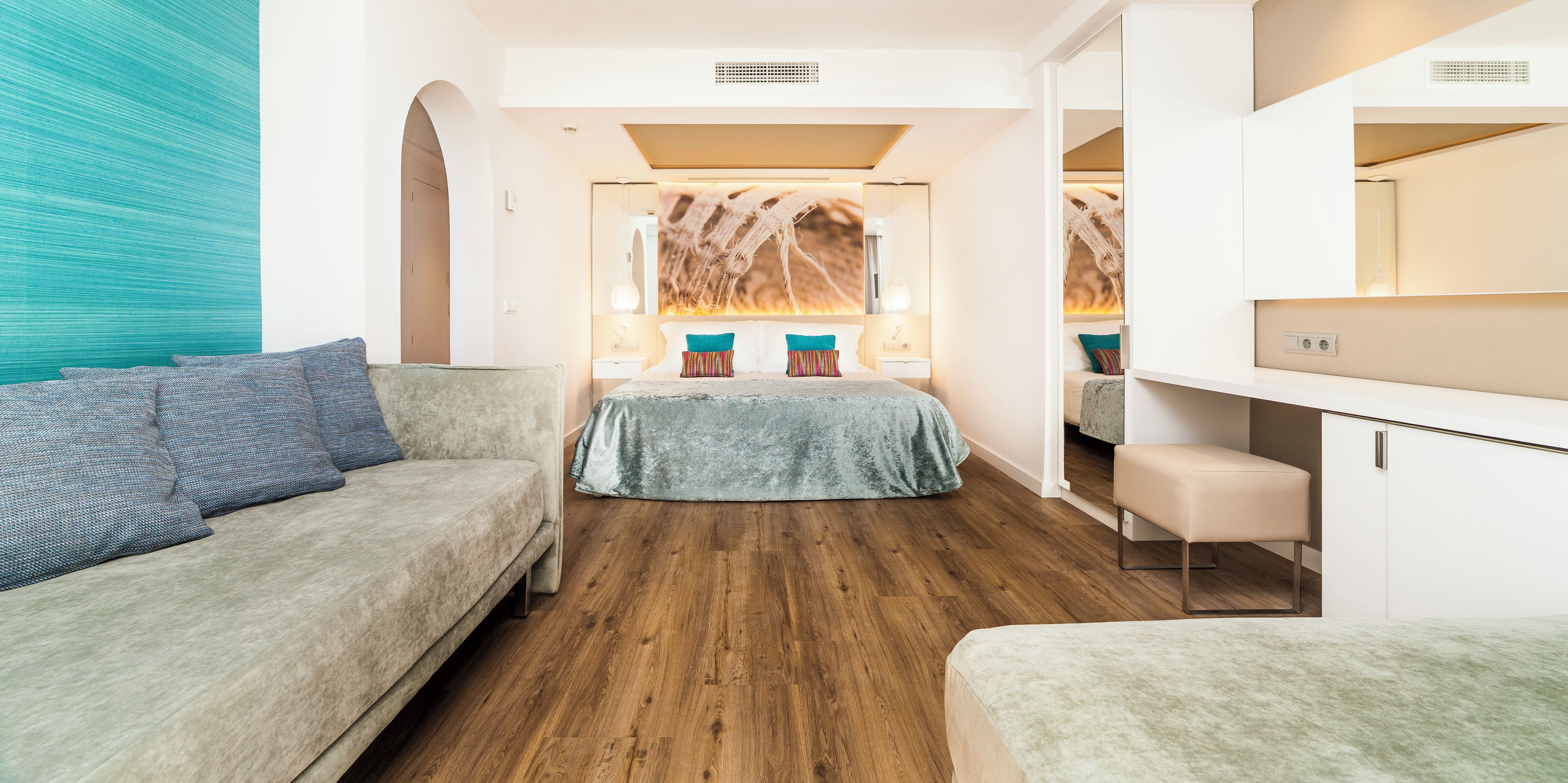Een moderne hotelkamer met houten vloer, een groot bed met kleurrijke kussens, een bank en een bureau.
