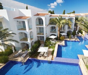 A resort with multiple swimming pools, white buildings with red-tiled roofs, and palm trees. - Insotel Tarida Beach Resort & SPA (Sant Josep de sa Talaia)