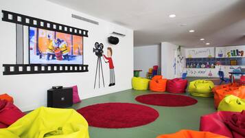 Una habitación de colores vivos con pufs, un mural con una franja de película y una pared con un personaje sosteniendo una cámara.