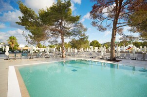 Un área de piscina con sillones de descanso y sombrillas, rodeada de árboles.