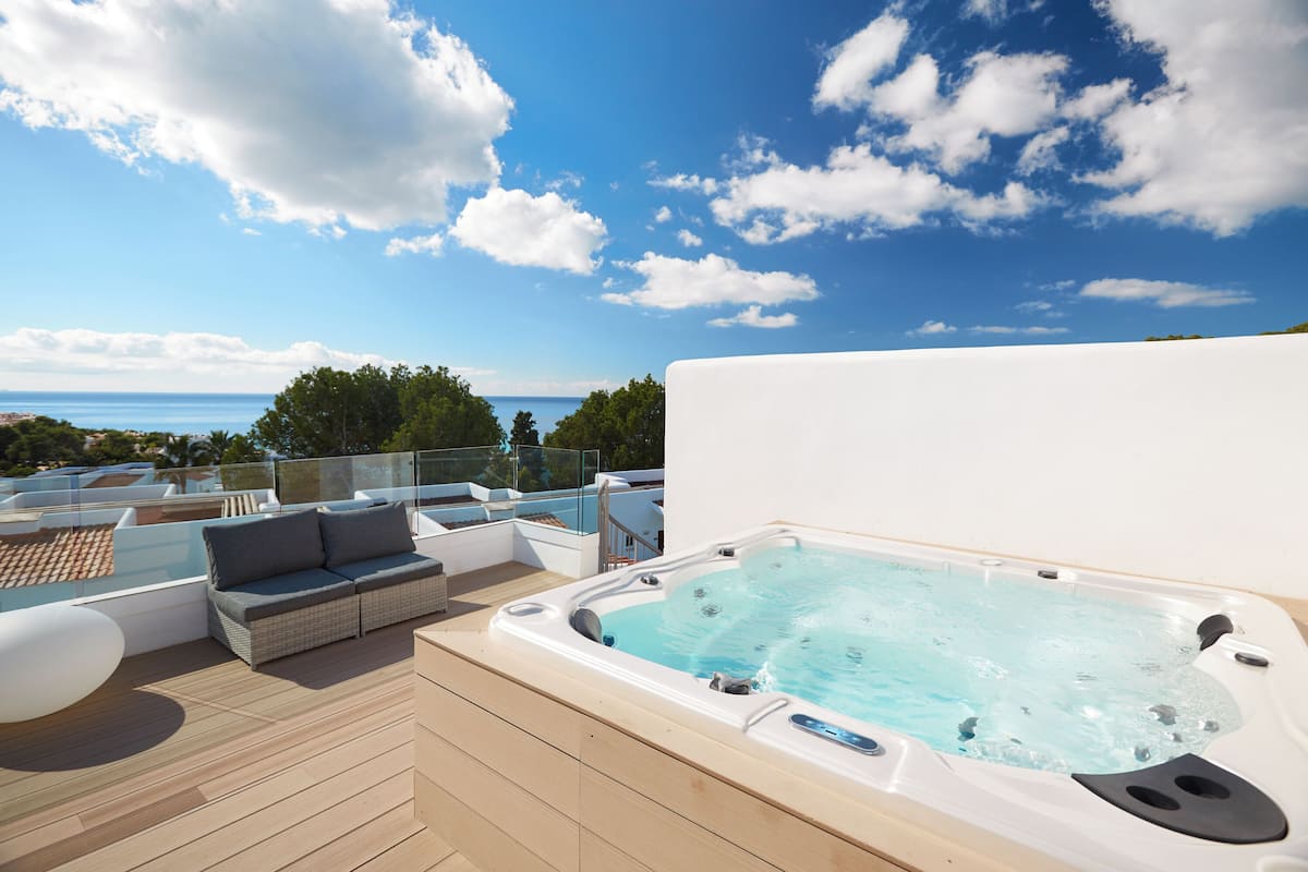 A rooftop deck with a hot tub, outdoor furniture, and a view of the sea.