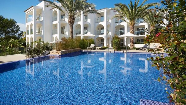A modern hotel with a large swimming pool, palm trees, and a clear blue sky. - Insotel Tarida Beach Resort & SPA (Sant Josep de sa Talaia)