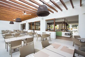 Un grand espace dédié à la salle à manger, avec plusieurs tables et chaises, un coin cuisine et une vue sur l’extérieur.