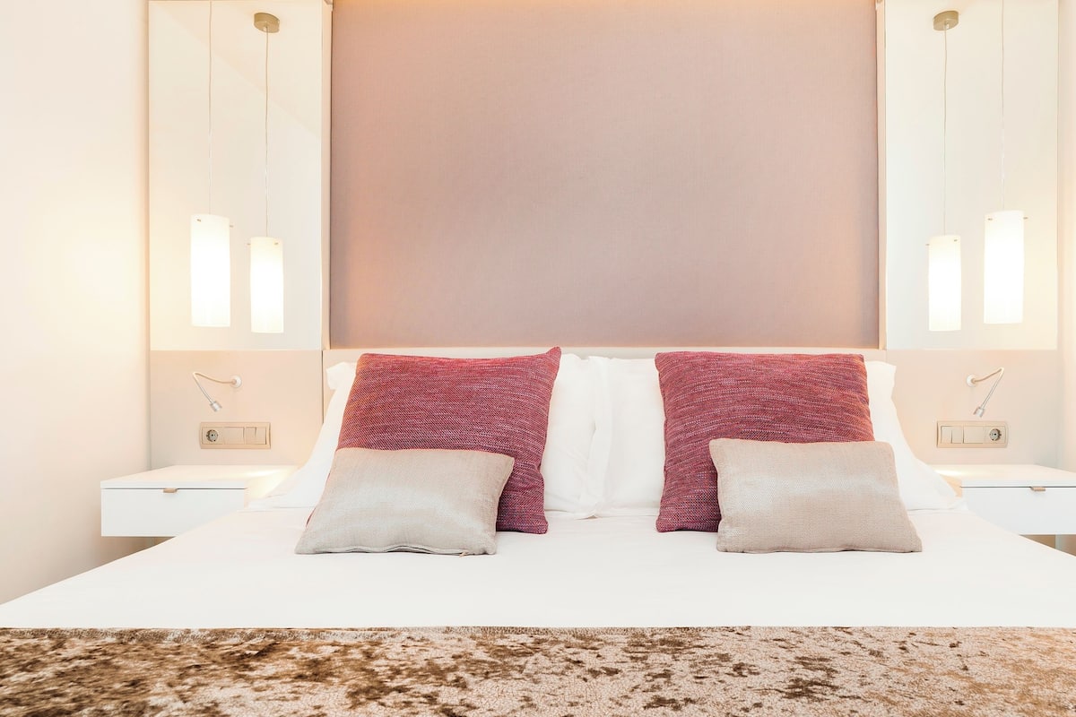 A modern hotel room with a large bed, two nightstands, and a large window with a view.
