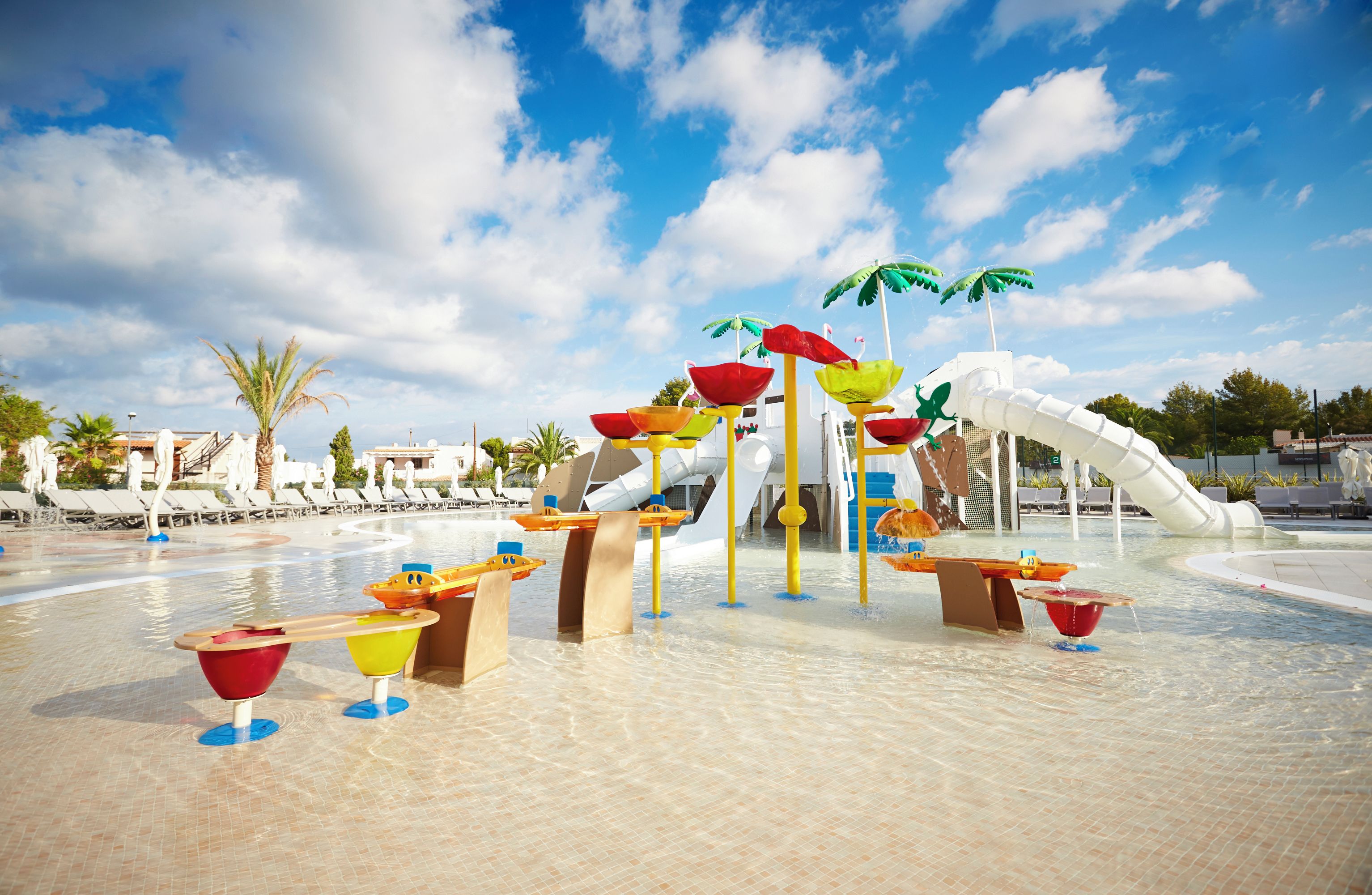 Een waterpark met glijbanen, palmbomen en ligbedden.