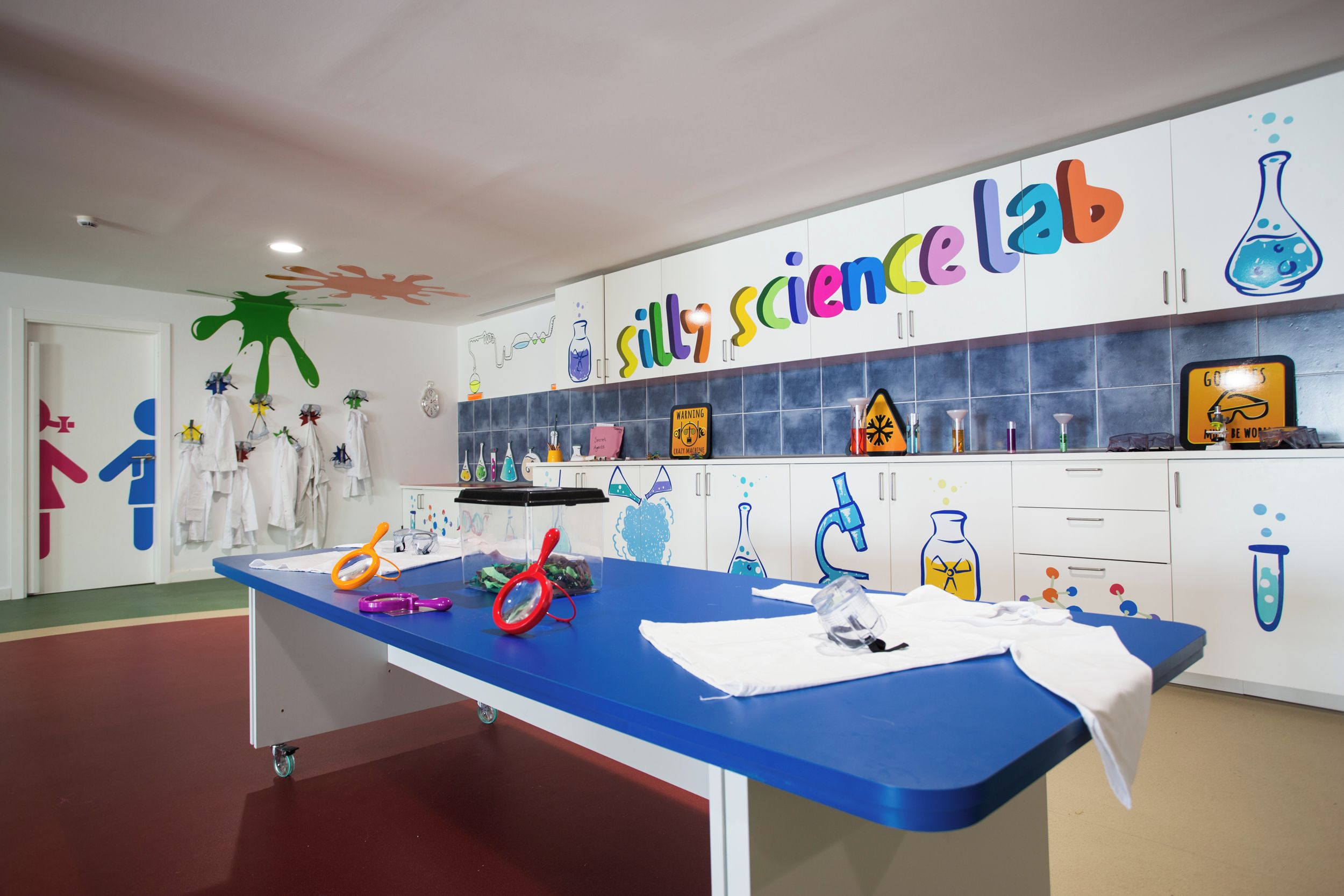 Een kinderkamer voor wetenschap met een blauwe tafel, witte kasten en vrolijke, leerzame decoraties.