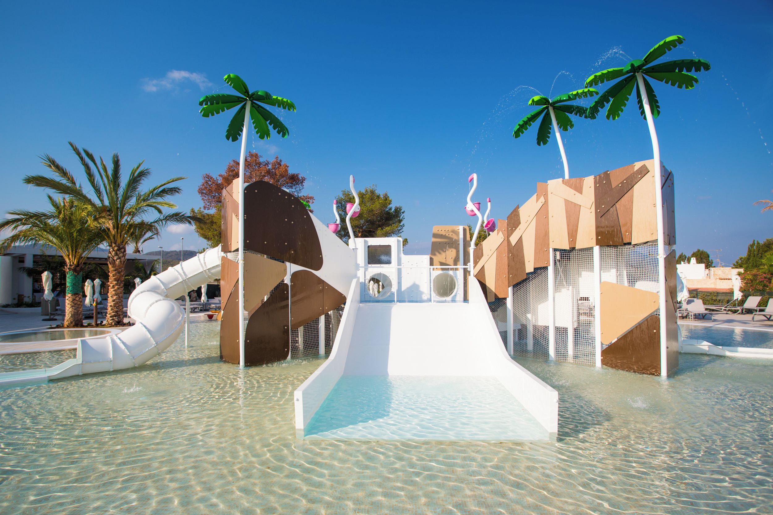 Un parco acquatico con uno scivolo bianco, palme e una piscina.