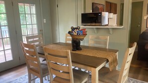Uma área de refeições com uma mesa de madeira, quatro cadeiras, um jogo americano trançado e uma tigela de petiscos sobre a mesa.
