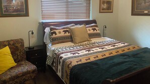 Quarto com cama, mesa de cabeceira, abajur e duas imagens emolduradas na parede.