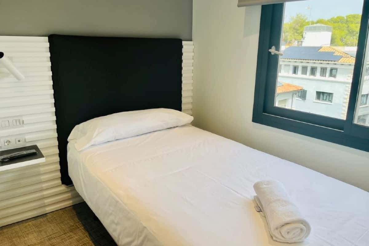 Una cama individual con ropa de cama blanca y cabecera negra en una habitación de hotel.