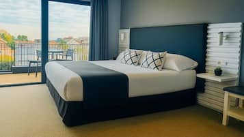 A modern hotel room with a large bed, a balcony with a view, and a small table with a plant.