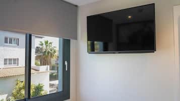 A room with a large window, a flat-screen TV mounted on the wall, and a view of neighboring buildings.