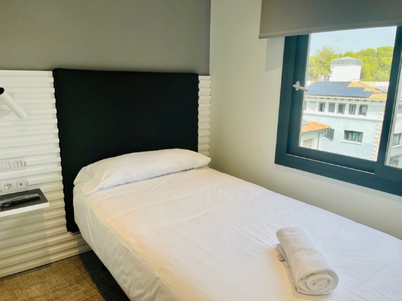 Una cama individual con ropa de cama blanca y cabecera negra en una habitación de hotel.