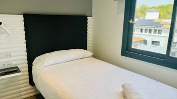 Una cama individual con ropa de cama blanca y cabecera negra en una habitación de hotel.