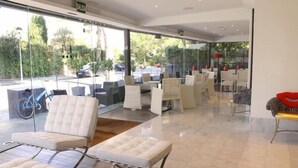 A modern indoor seating area with cushioned chairs and tables, large windows offering a view of the outdoors. - Sitges (Sitges)