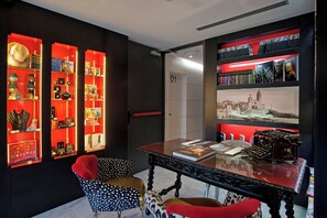 Una habitación con una mesa de vidrio, estanterías rojas y negras con diversos objetos, y una puerta con la inscripción '01'.